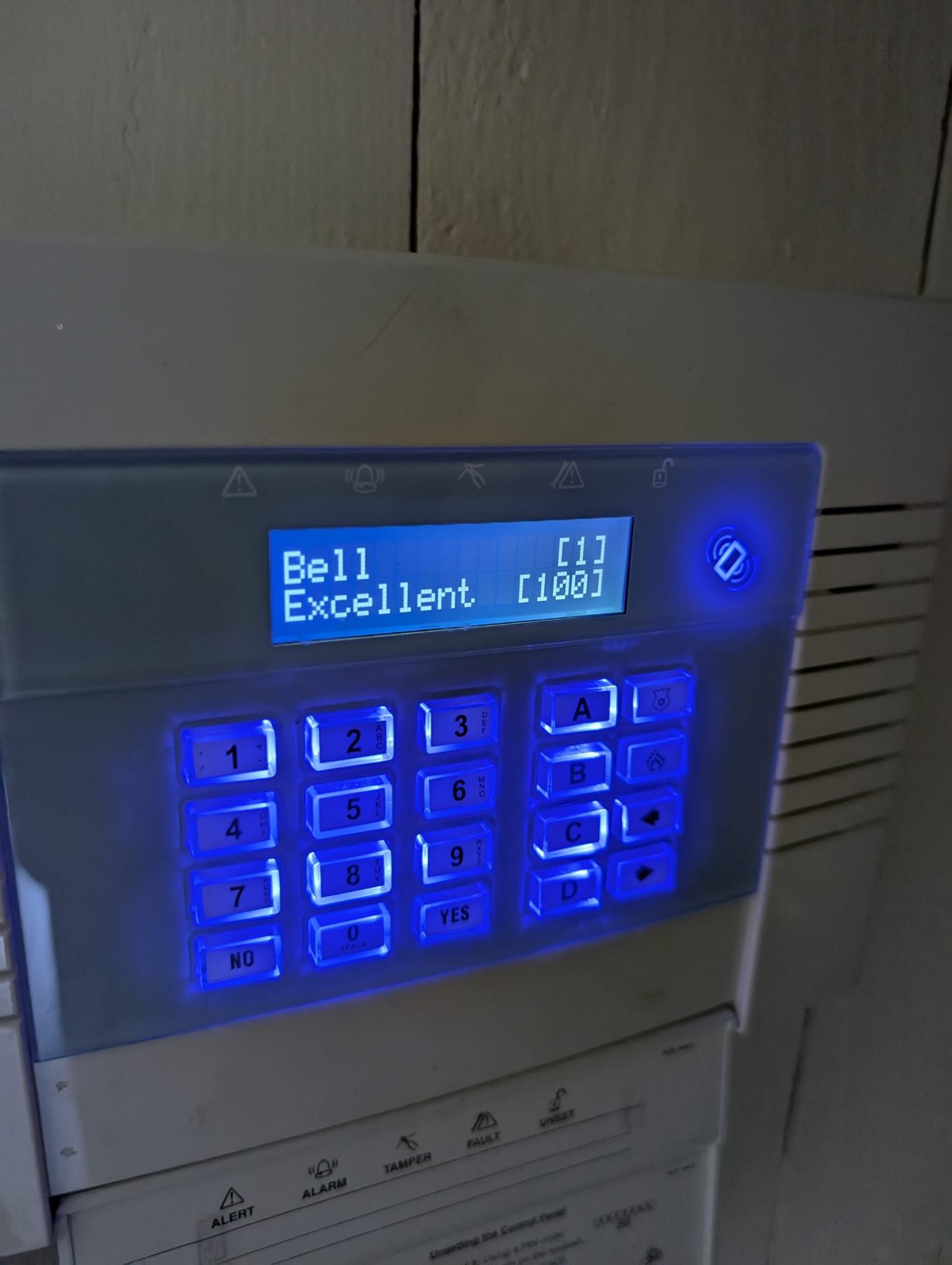 Intruder alarm keypad with blue backlight installed on a wall in a London home